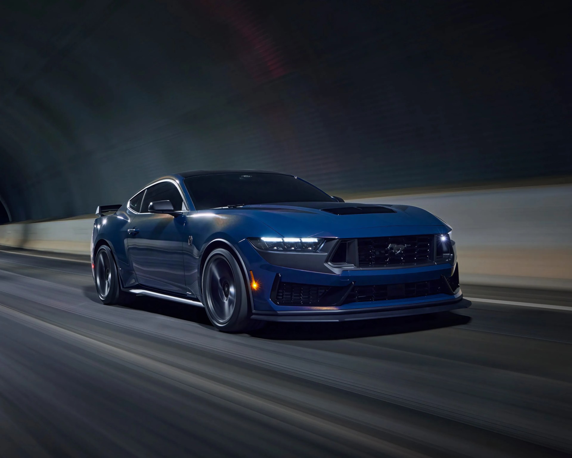 Το μπλε Ford Mustang Sports Car που οδηγεί μέσα από μια σήραγγα τη νύχτα, με προβολείς και πρόβλεψη κίνησης στο δρόμο.